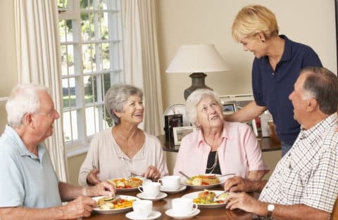caregiver and a group of elderly chatting on a meal
